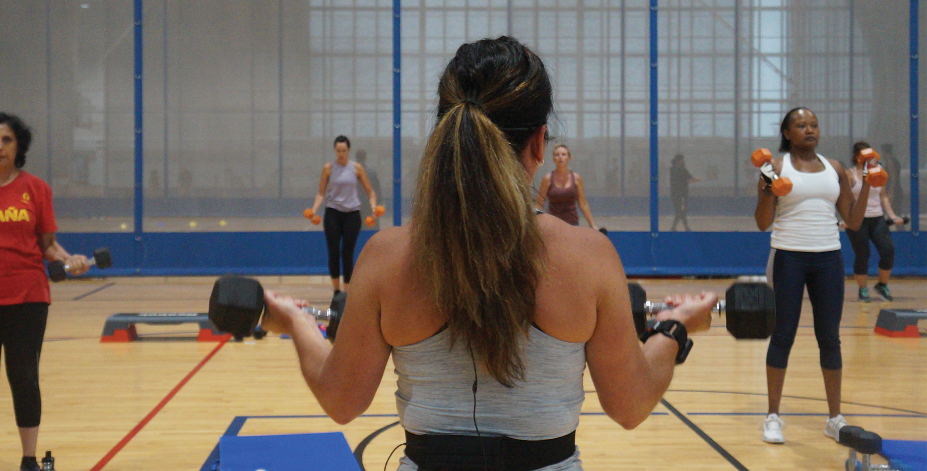 A group workout on court in the fieldhouse lifting dumbbells