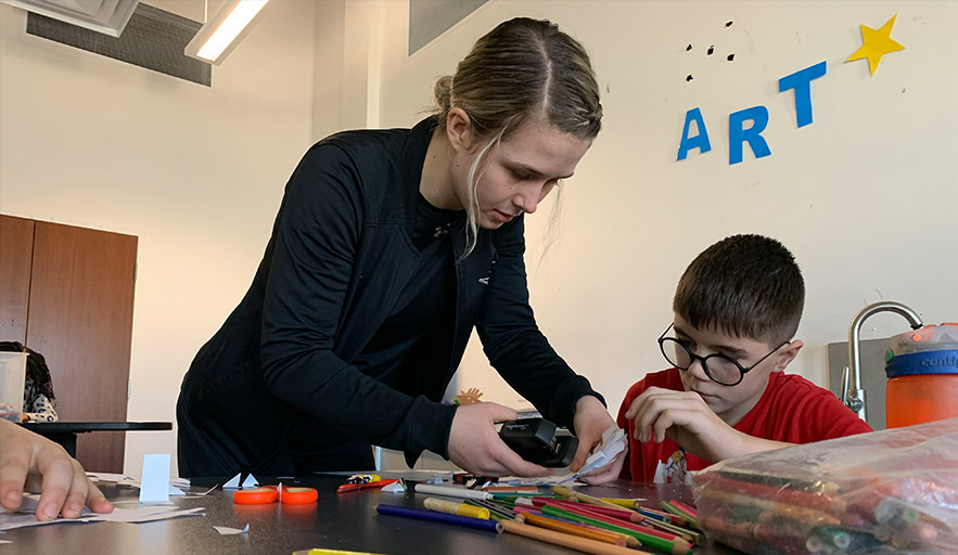 Abilities Centre program coordinator instructing and assisting youth participant with art and craft program 