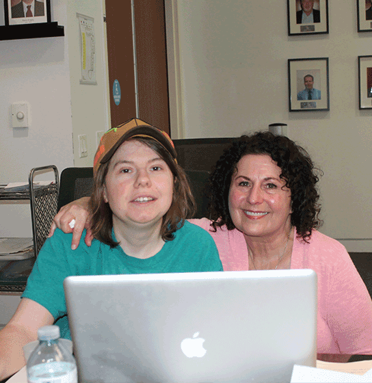 Two participants of the program smile behind a laptop sitting at a table 