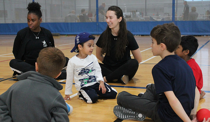 Program coordinator sitting on court floor with youth participants ready to start new program