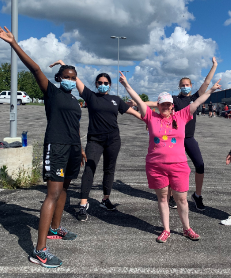 Staff and participants stand with their hands up in the air excited to be back in parking lot programs on a sunny day